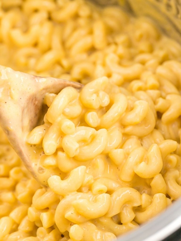 Close up picture of cheesy elbow pasta in the Instant Pot with a serving spoon.