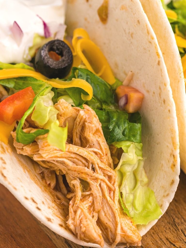 Close up shot of a taco with chicken, lettuce, tomatoes, and olives inside of the taco shell.