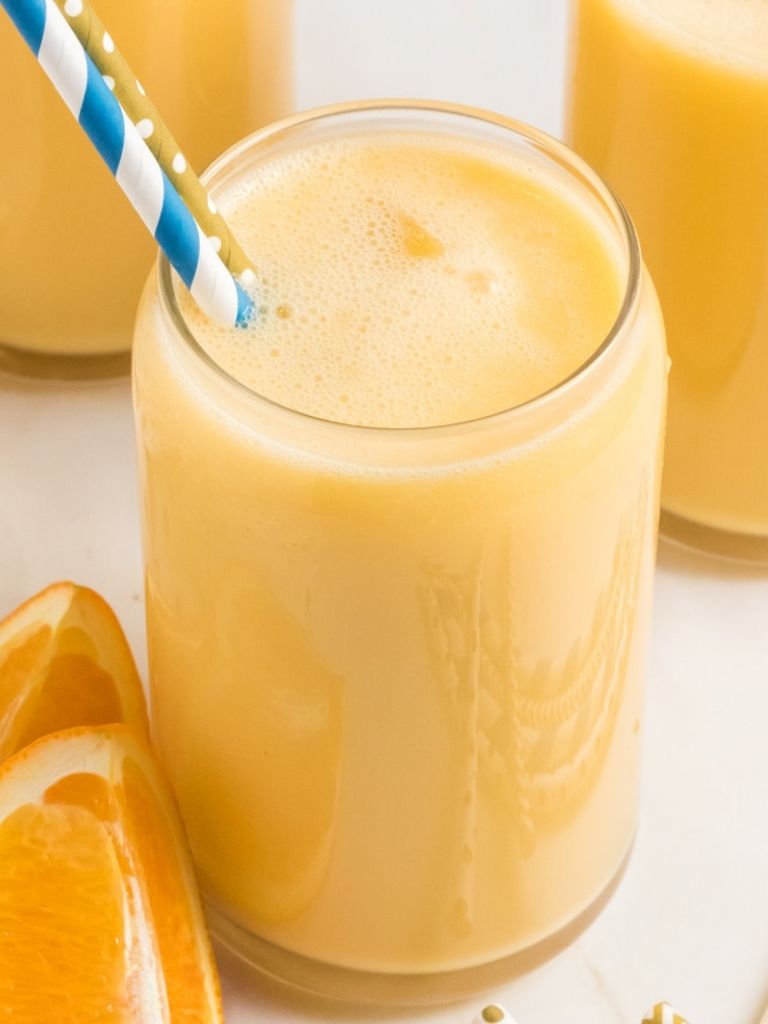 A cup of orange smoothie with an orange on the rim of the glass cup. 