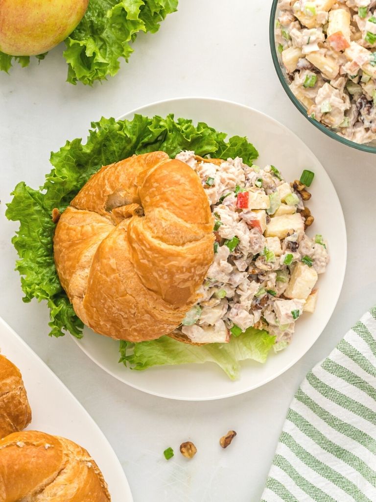 Overhead shot of croissant with chicken salad inside of it with a green cloth background.
