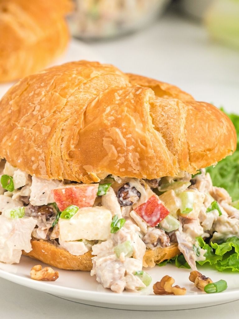 A white plate with a croissant and chicken salad inside of it. 