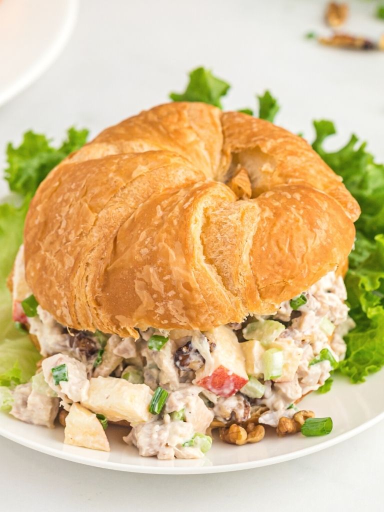 A croissant with chicken salad and green leaf lettuce against a white background.