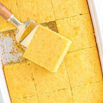A white pan with cornbread inside of it with a spatula picking up a piece of it.