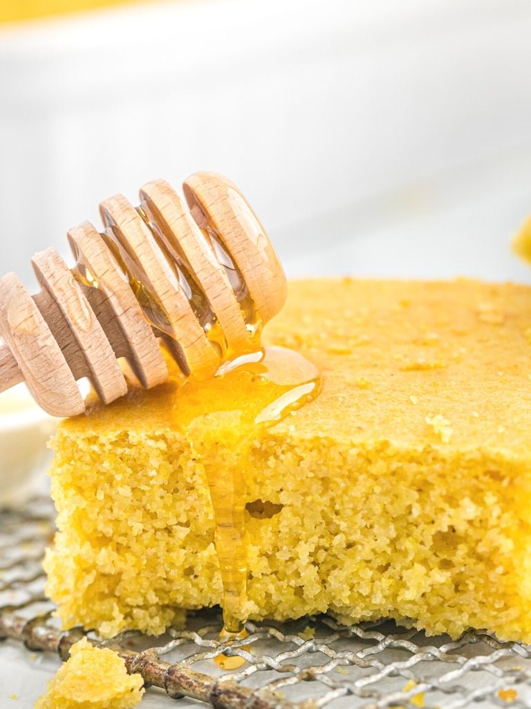 Slice of cornbread with honey dripping on it sitting on a wire cooling rack. 