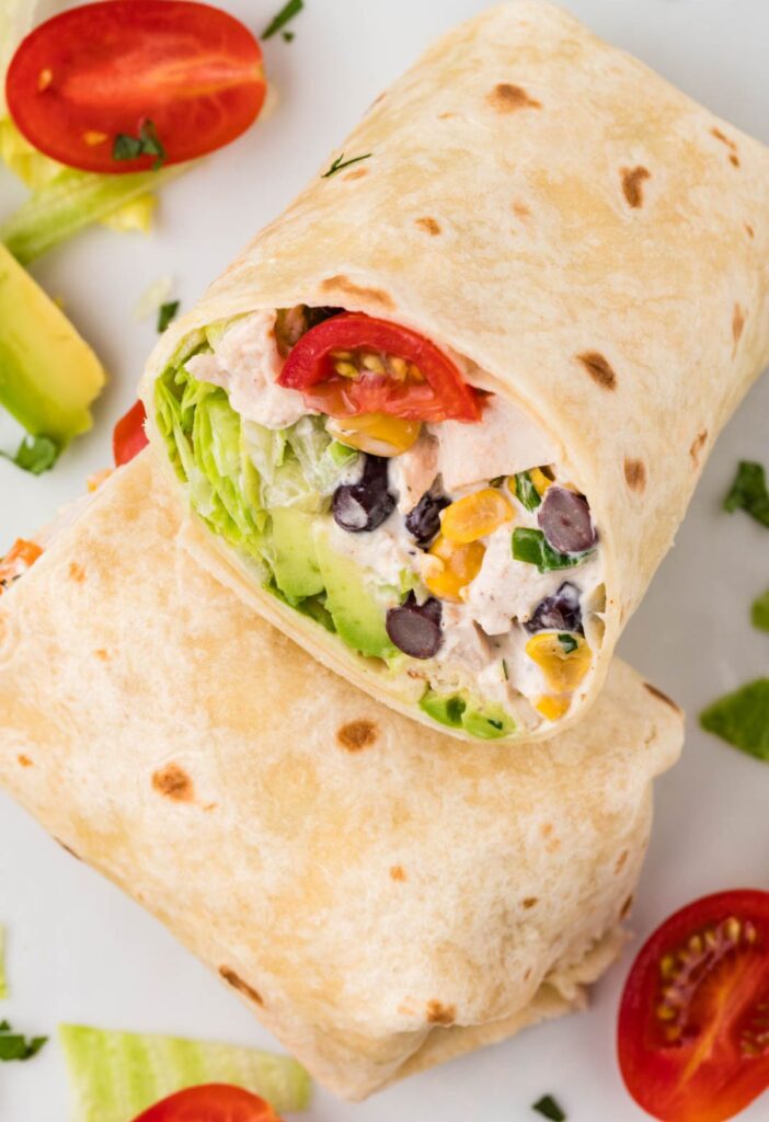 Stack of wraps on a plate with tomato and avocado slices next to it.