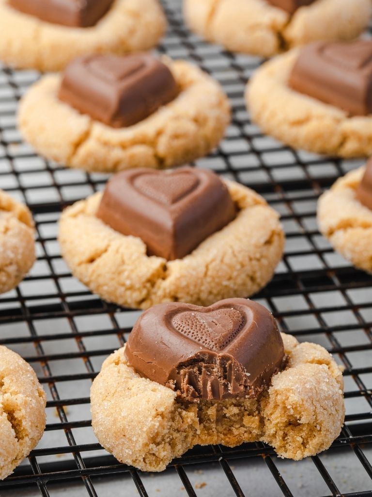 A rack of peanut butter heart cookies with one cookie with a bite taken out of it to show the middle.