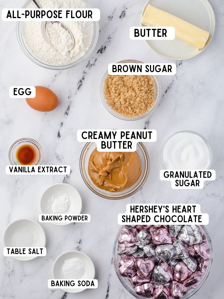 Ingredients needed to make peanut butter heart cookies laid out on a white background with a text box above each one with the name of it. 