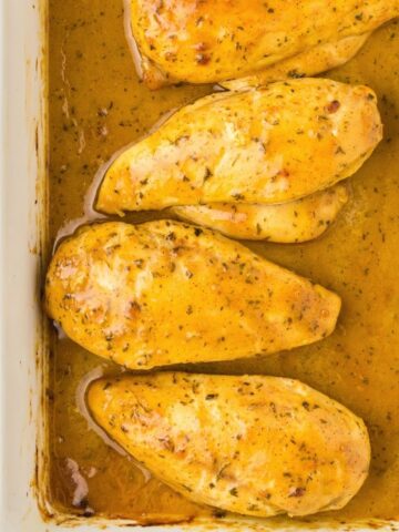 Four chicken breasts inside a white pan, cooked, and covered in a mustard honey sauce.