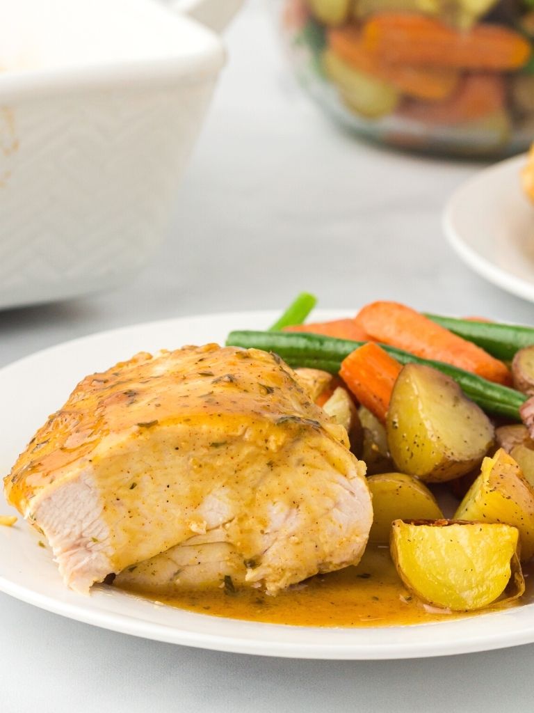 Slice of chicken with sauce over it showing the inside of the chicken breast on white plate with vegetables next to it. 