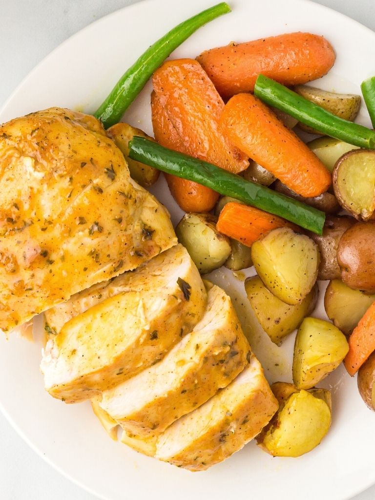 A plate with chicken breast on it, sliced, next to some roasted vegetables. 