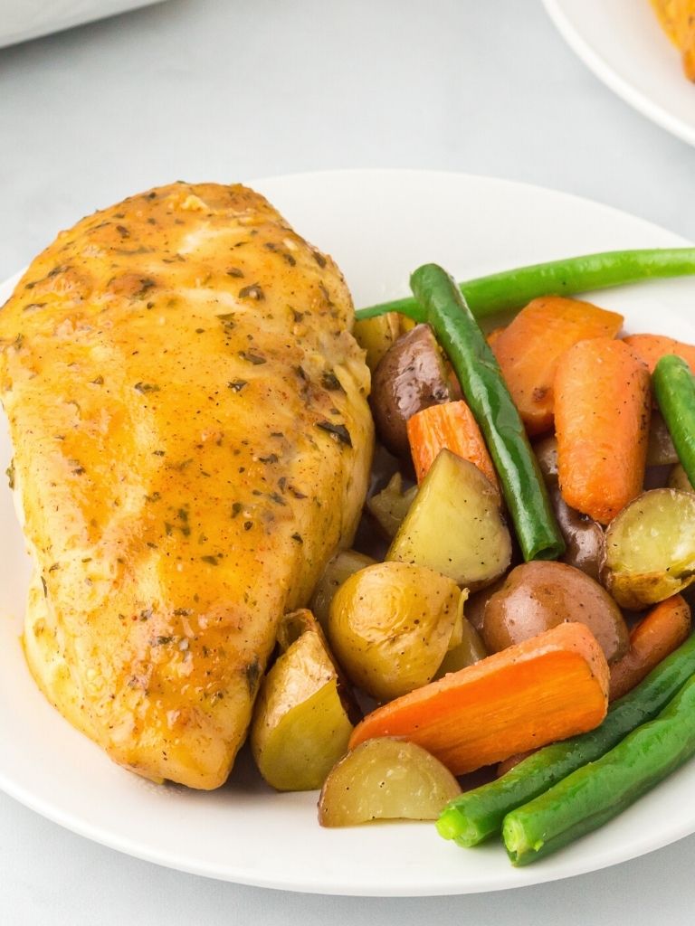 Chicken breast on a plate with cooked vegetables.