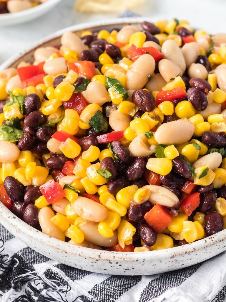 Bean salad inside a bowl with a black and white cloth next to it. 