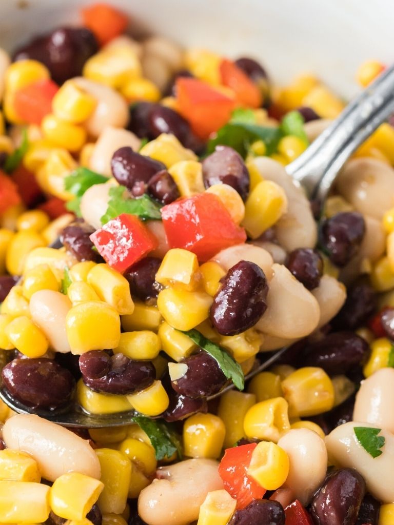 A spoonful of salad with corn and black beans inside a white bowl. 