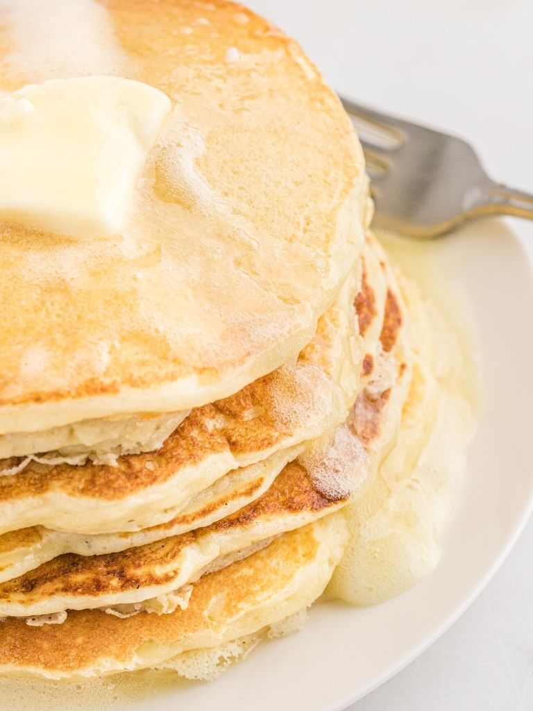 Stack of pancakes on a white plate with butter and syrup.