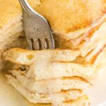 A fork inside a stack of pancakes with syrup on top.