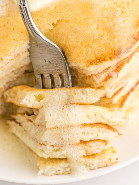 A fork inside a stack of pancakes with syrup on top.