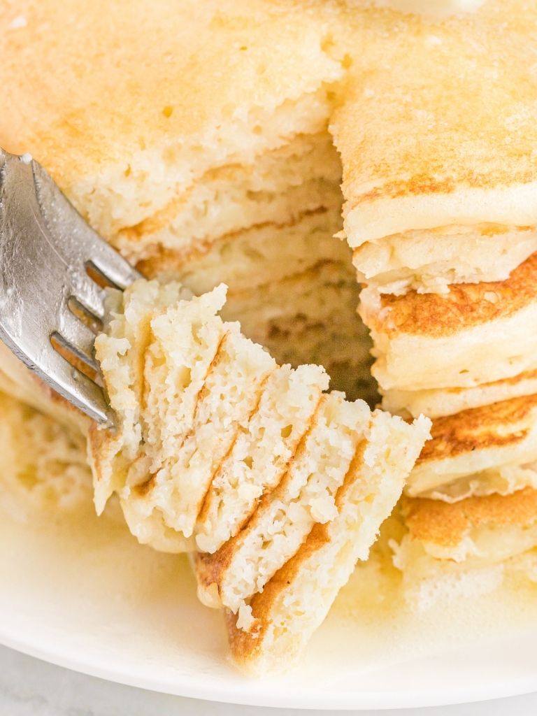 A fork inside pancakes with some pieces on it ready to eat. 