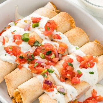 A white dish with taquitos inside of it and topped with sour cream and tomatoes.