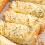 Slices of garlic bread with cheese on a parchment paper lined tray.