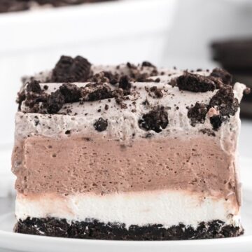 Four layers of an oreo dessert recipe, a piece of it is sitting on a white plate.