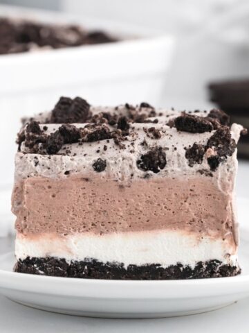 Four layers of an oreo dessert recipe, a piece of it is sitting on a white plate.