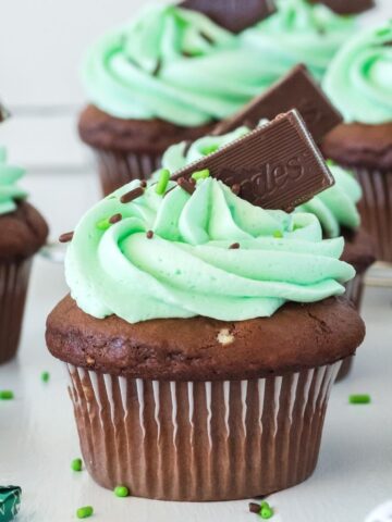 A mint chocolate cupcake on a white plate topped with frosting and garnished with sprinkles and mint candy.