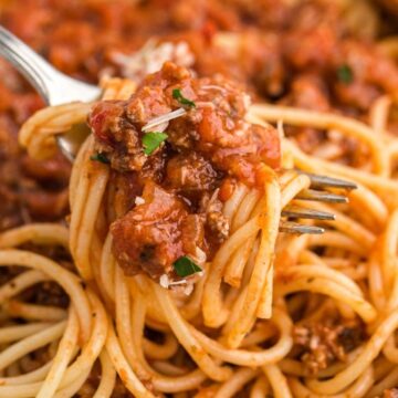 A fork with pasta intertwined on it with a bowl of the past in the background.