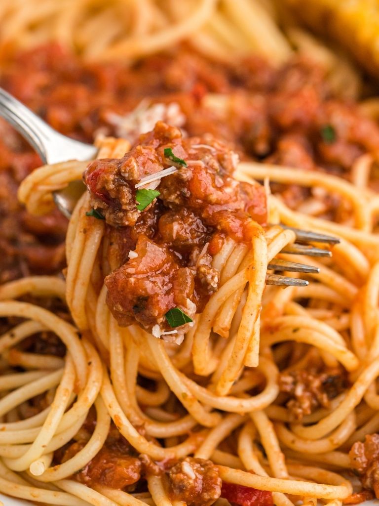 A fork with pasta intertwined on it with a bowl of the past in the background.