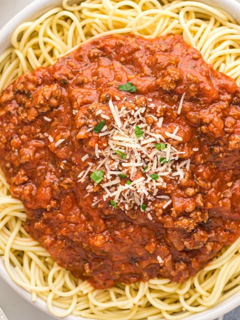 Close up shot of pasta sauce over some spaghetti noodles in a white bowl. 
