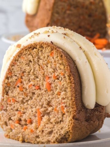 A slice of carrot cake with frosting sitting atop a white plate.