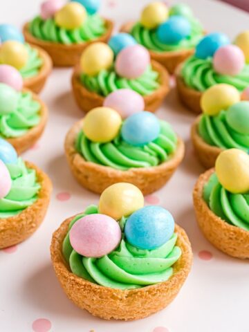 Easter Basket Sugar Cookie Cups are made in a muffin pan with prepared sugar cookie dough as the basket base, filled with vanilla buttercream, and topped with chocolate eggs. A fun, cute, and festive treat that everyone will love. 