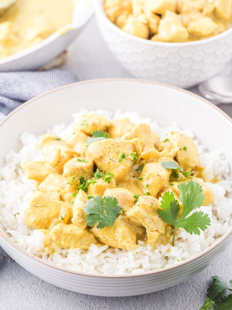 Bowl with white rice in it topped with chicken and a curry sauce.
