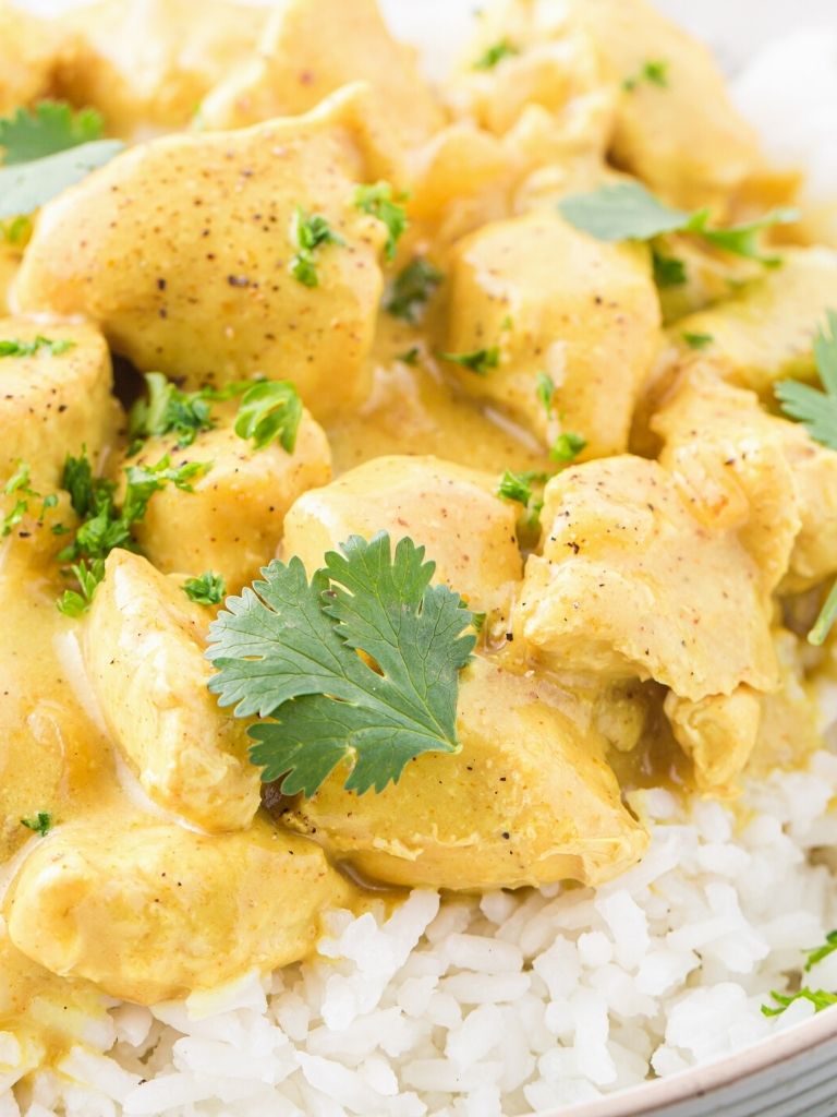 Chunks of chicken with a curry sauce served over rice in a white speckled serving bowl.