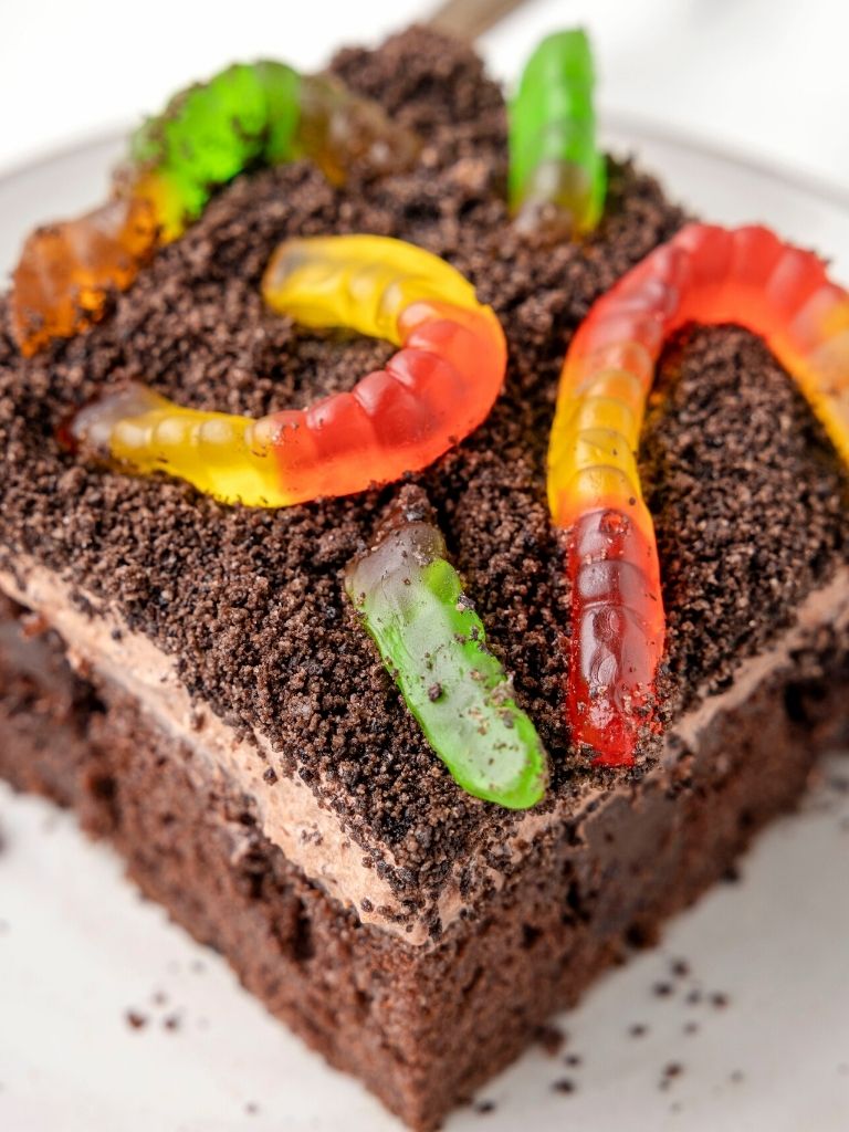 A piece of Oreo dirt cake on a white plate with crushed cookies and gummy worms.