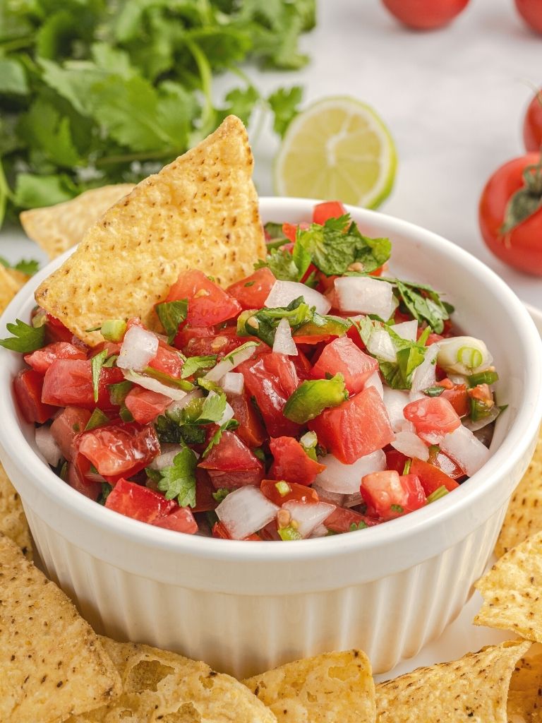 Chopped tomatoes, onion, jalapeño inside a white serving bowl with a chip on top of it.