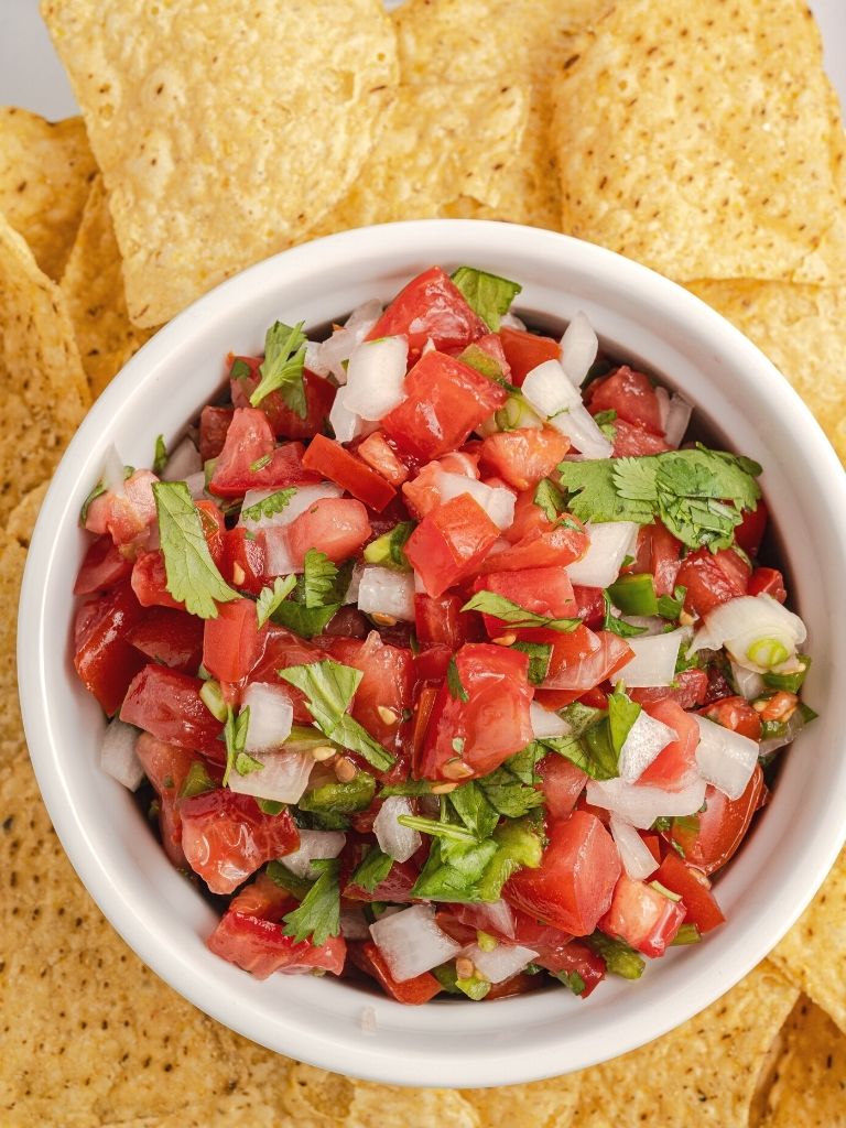 salsa inside a bowl with tortilla chips surrounding it. 