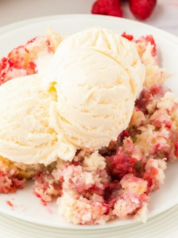 Raspberry cobbler on top a stack of white plates with a scoop of ice cream on top of it.