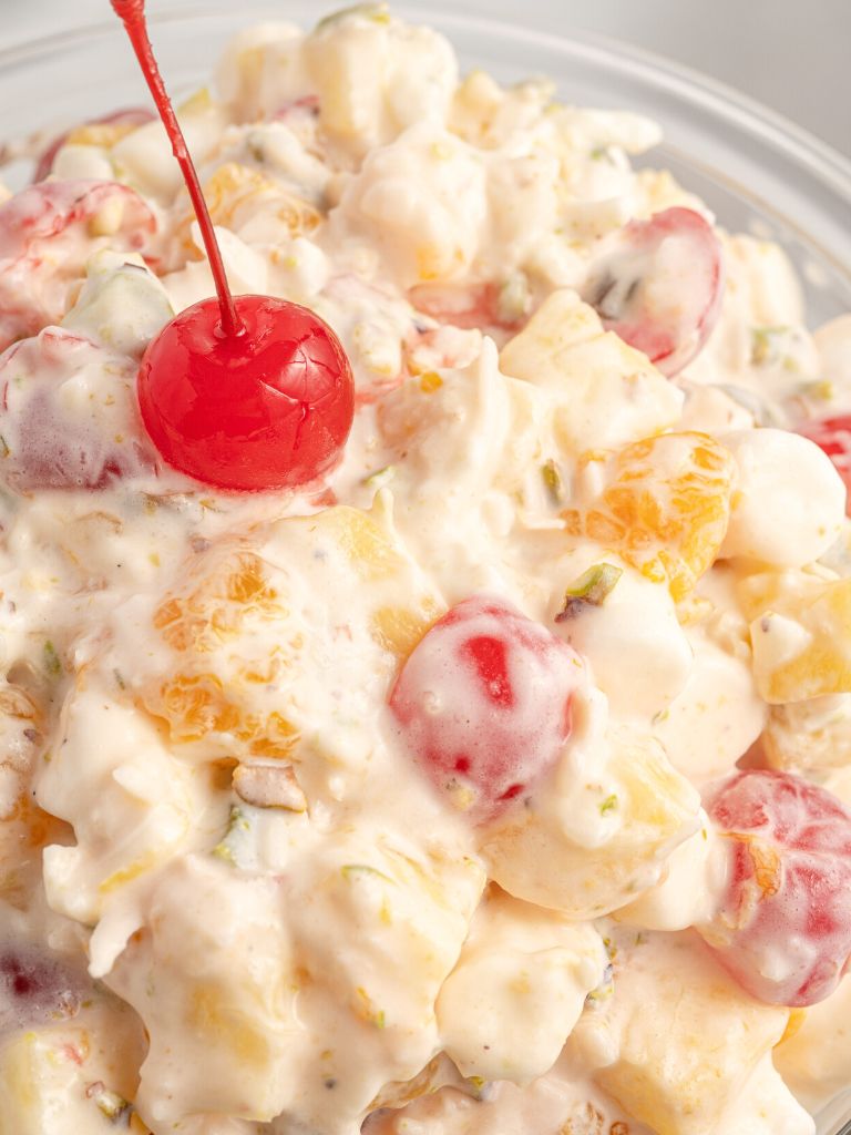 Close up of a creamy fruit salad with a cherry on top.
