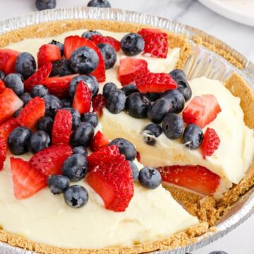 A cream pie with fresh berries inside a graham cracker crust cut into slices.