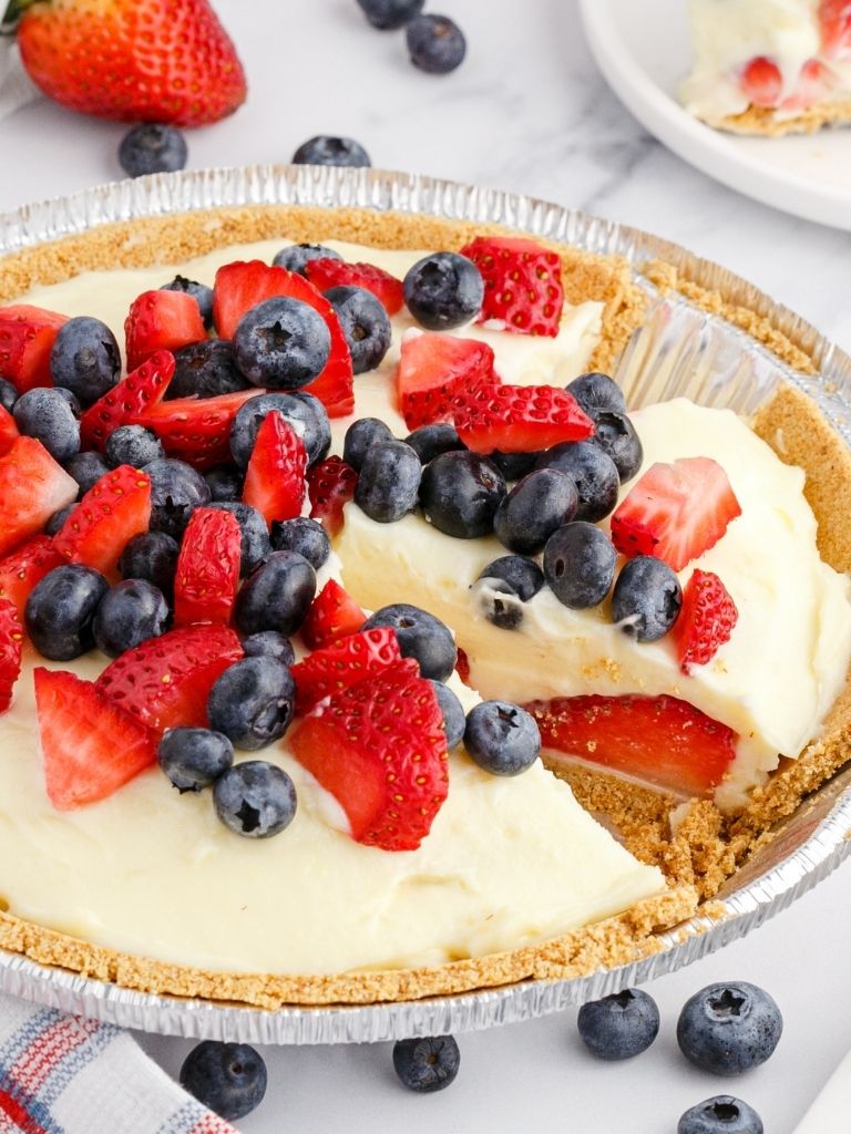 A cream pie with fresh berries inside a graham cracker crust cut into slices.