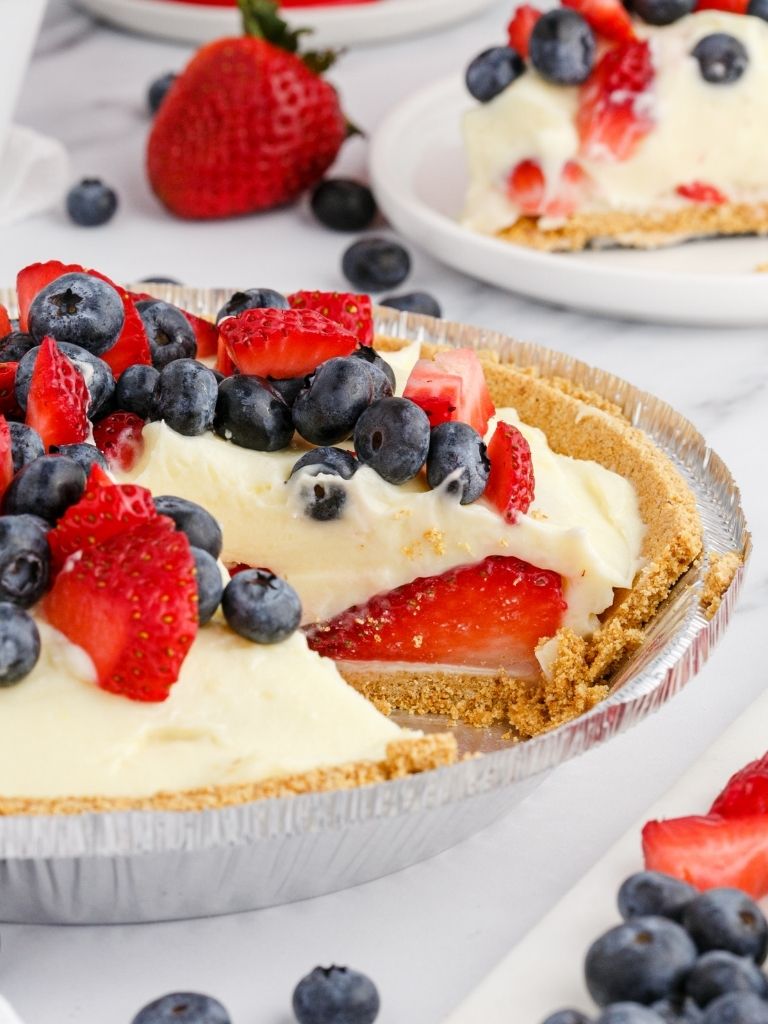 Side shot of a berries cream pie topped with fresh berries inside a pie crust. 