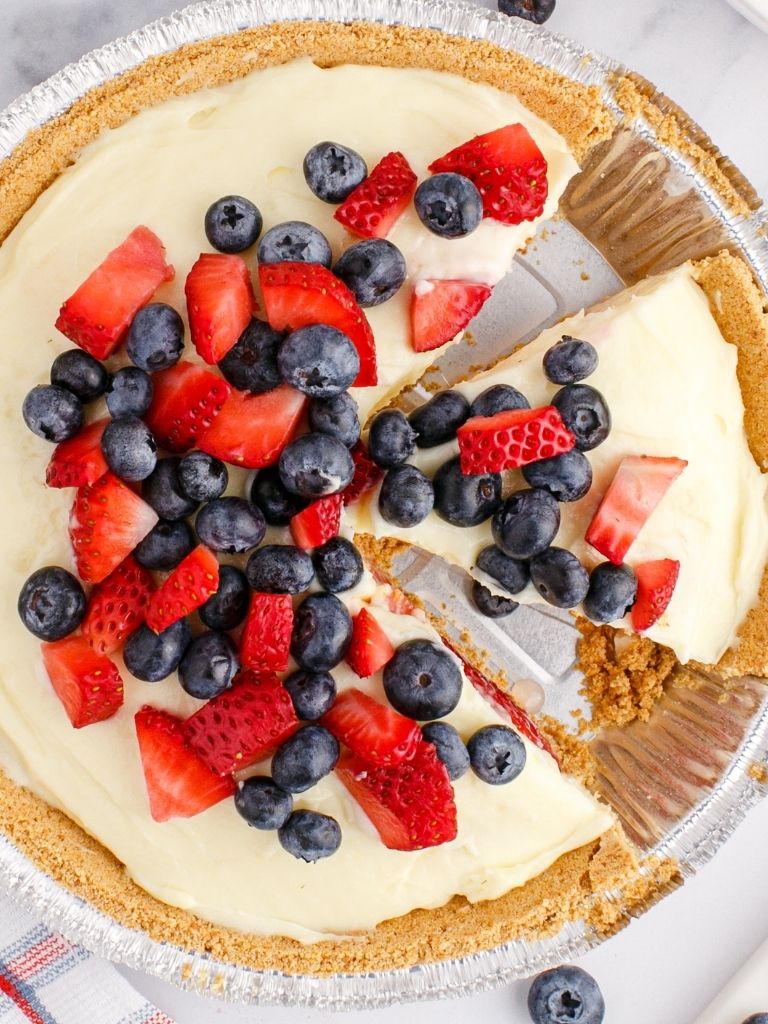 Overhead shot of a cream pie with berries and cream. Sliced into pieces inside the foil crust plate. 