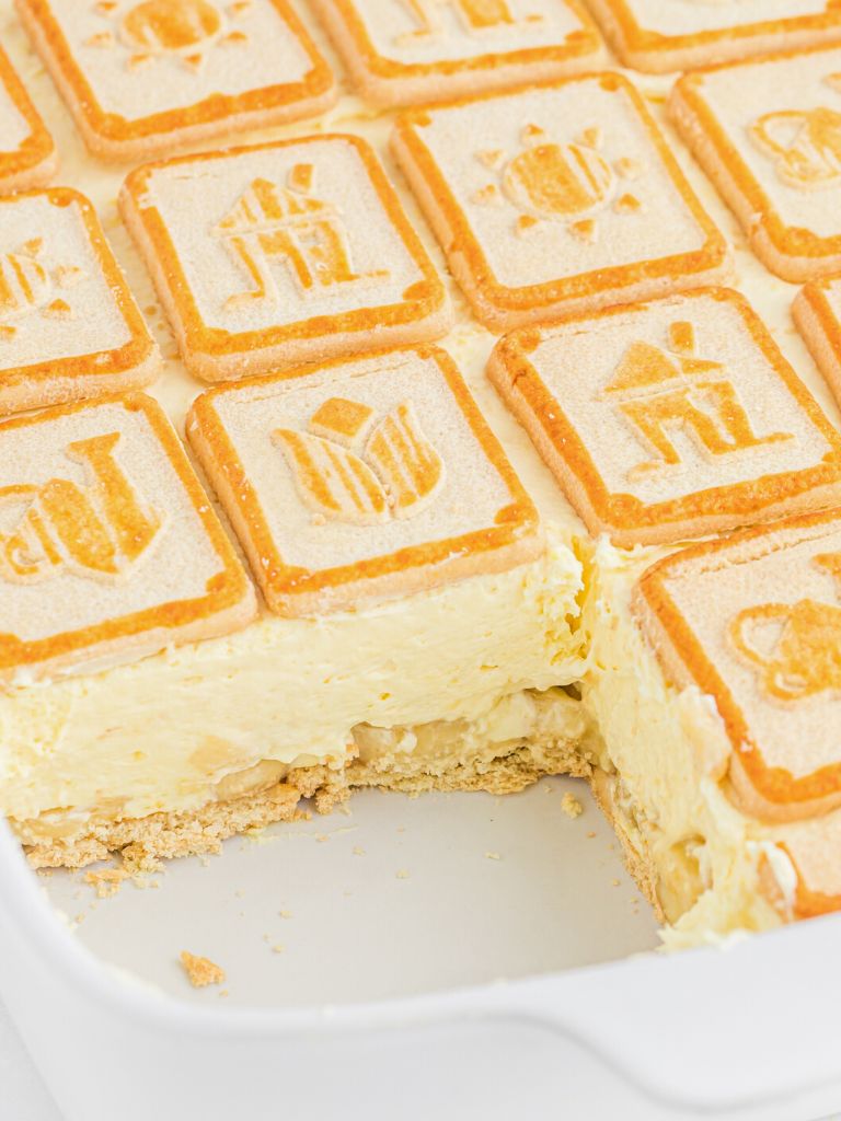 White dish with banana pudding dessert inside of it with chessmen butter cookies, pudding, and sliced bananas.