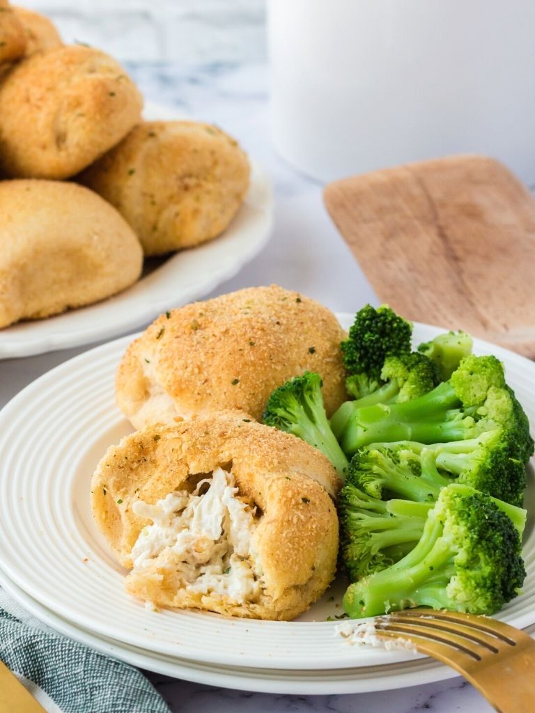A white plate with broccoli on it and a chicken pillow that has been cut in half. 