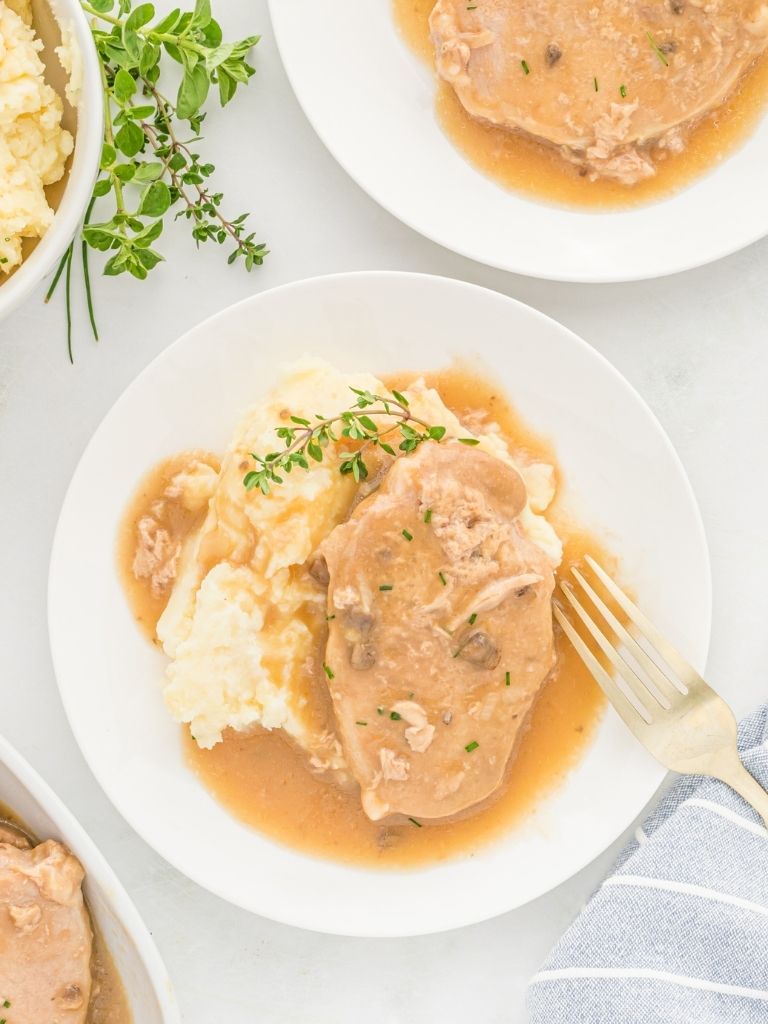 Overhead shot of a plate of pork chops over mashed potatoes topped with a cream of mushroom gravy. 