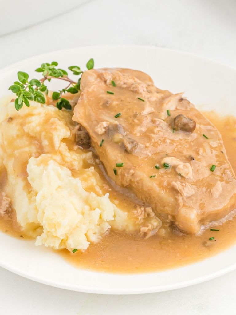 A white plate with a cream of mushroom pork chop sitting on top of mashed potatoes.