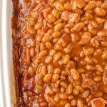 Baked beans inside a white baking dish. Close up shot showing texture.