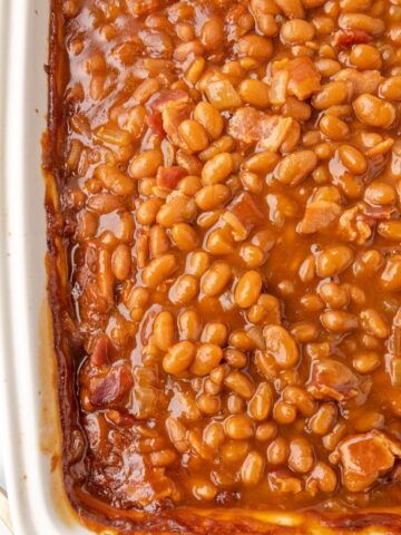 Baked beans inside a white baking dish. Close up shot showing texture.