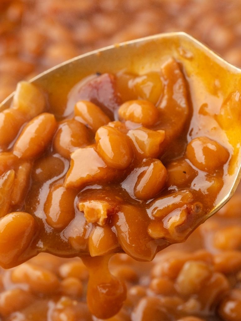 Close up shot of beans on a spoon with sauce dripping off of the spoon.