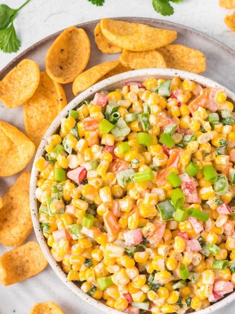 Corn salad with ranch inside a white bowl with Fritos corn chips around it.